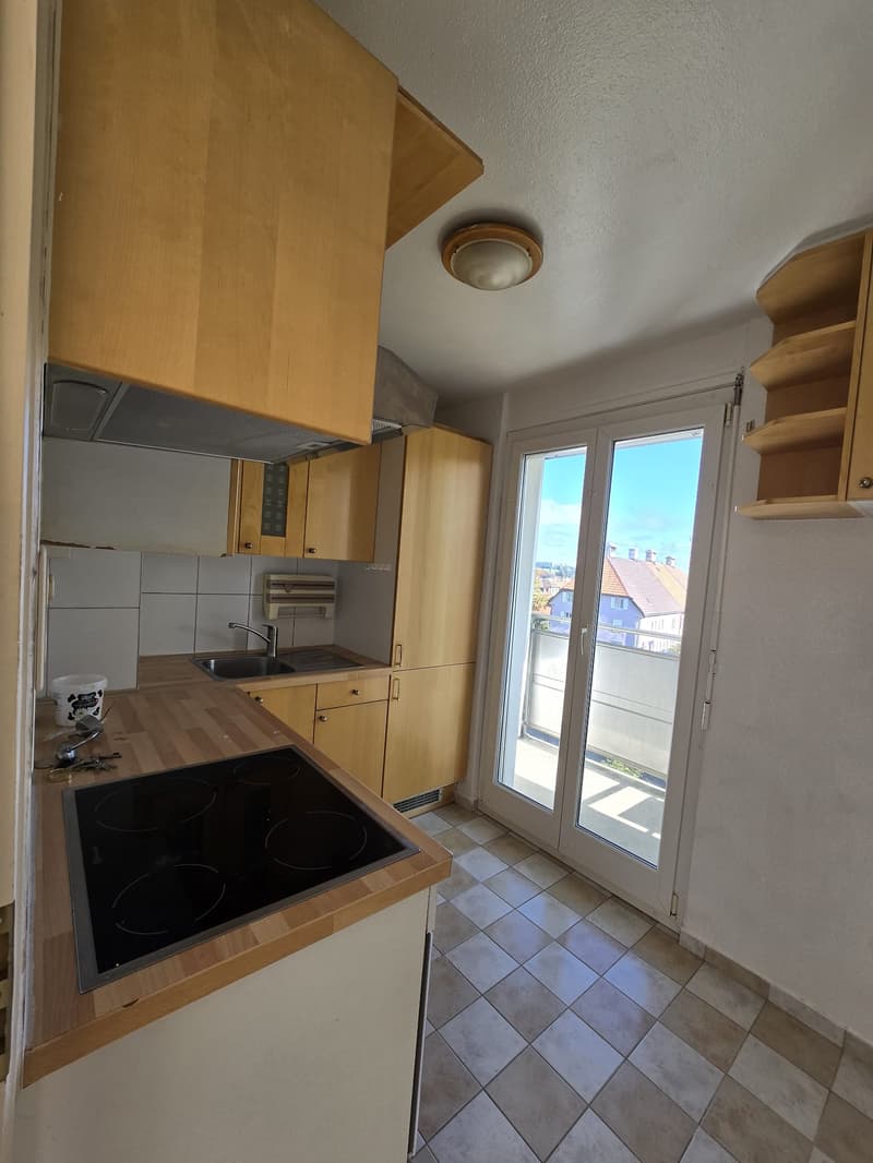 modern kitchen with wooden cupboards, tile floor, large window to balcony with city view