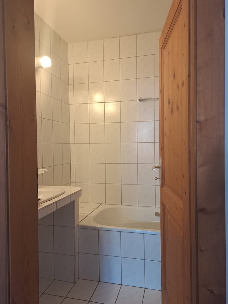 white tiled walls, white bathtub, white sink, wooden door, mounted towel bar