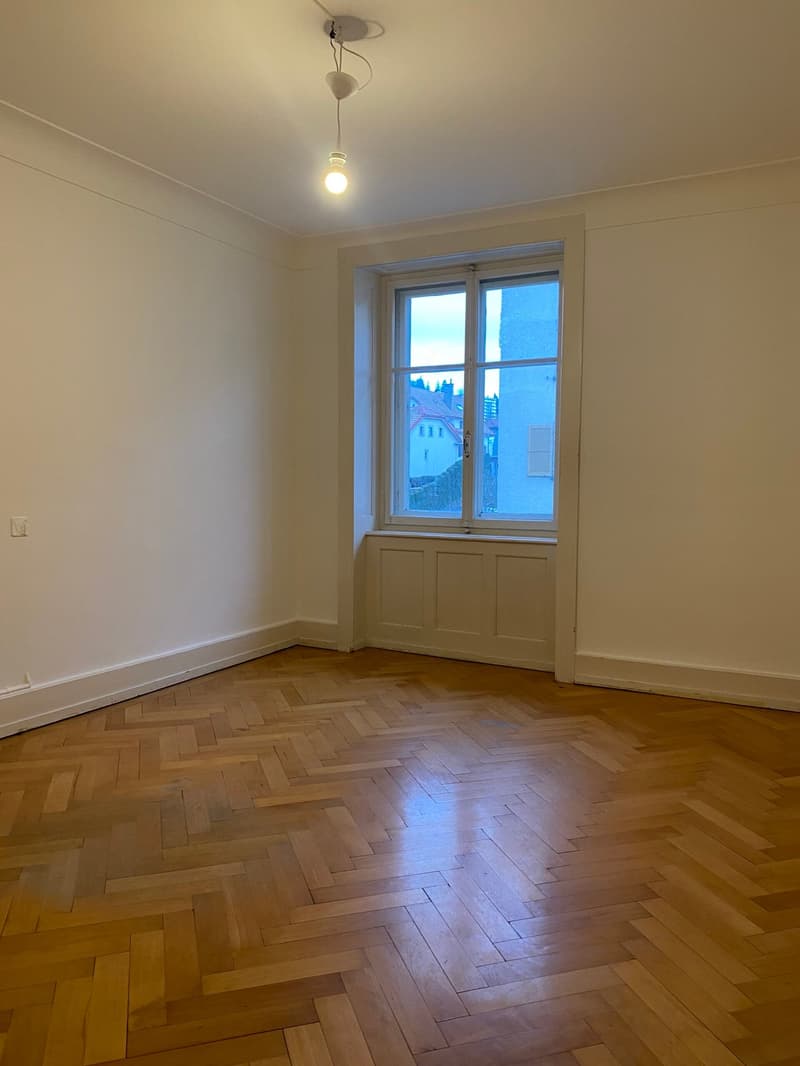 Empty room with wooden herringbone floors, large window with view, white walls and ceiling