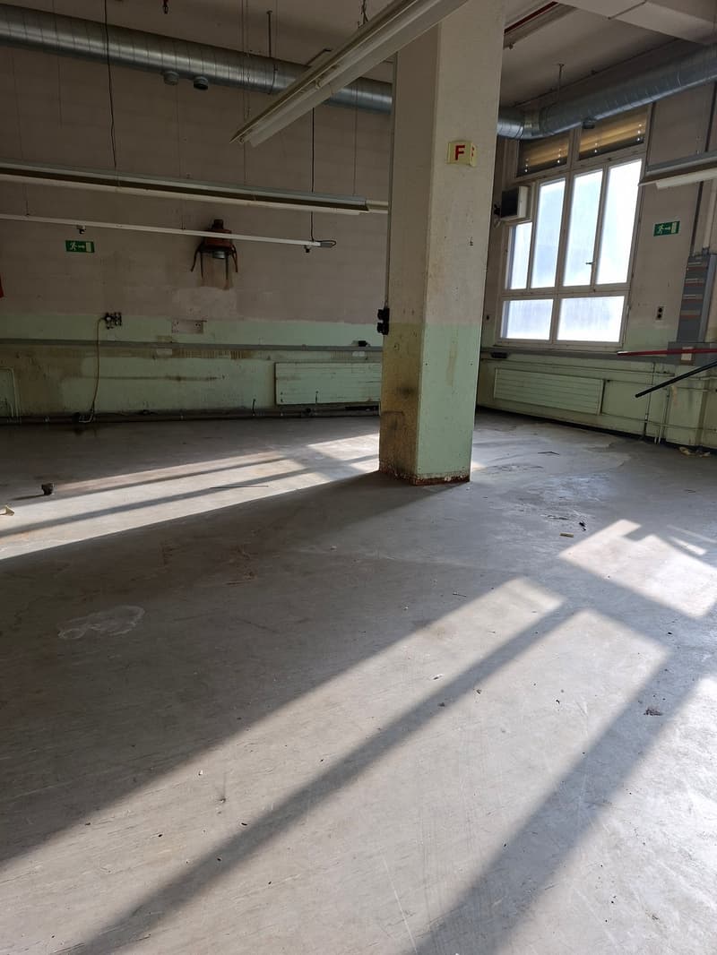 large open space with pipes on ceiling, concrete floor, radiators against walls, windows with grills