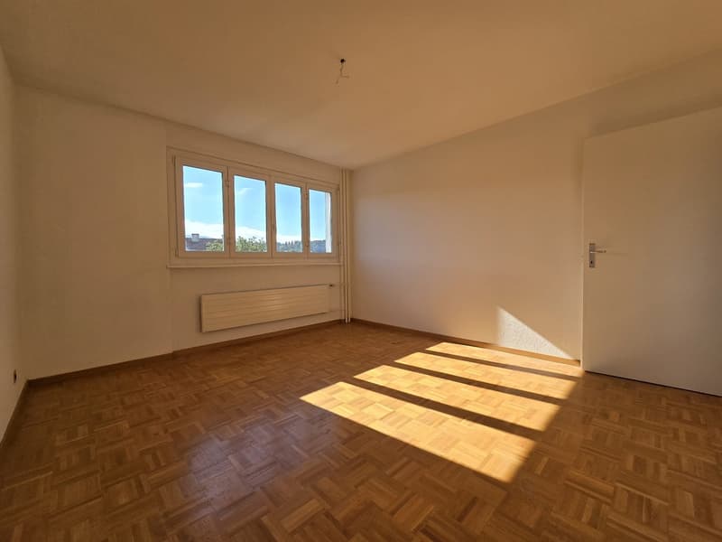 Empty room with hardwood floors, large windows, white walls, radiator.