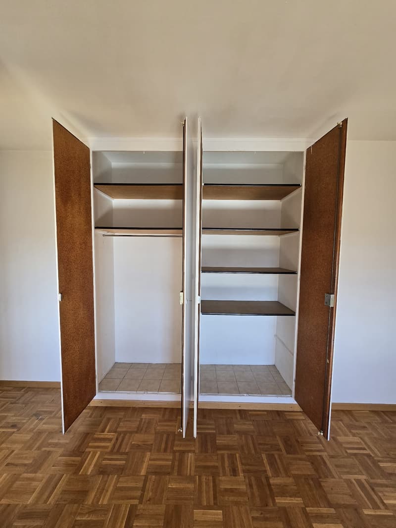 A fully open double-door wooden wardrobe with wooden flooring and tiled flooring inside.