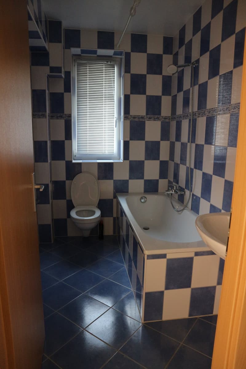 A bathroom with a bathtub, a toilet, and a sink, with blue and white checkered tiles on the wall and floor.