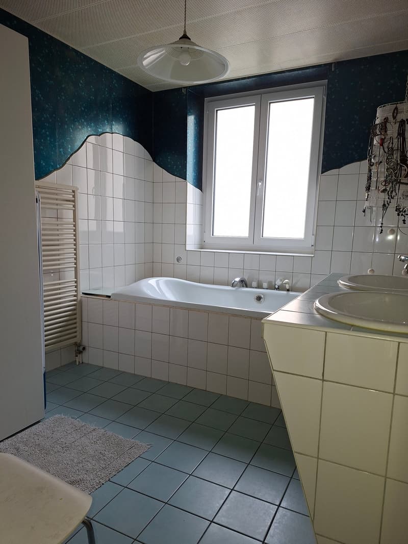 A bathroom with bathtub, sink, radiator and tiled walls