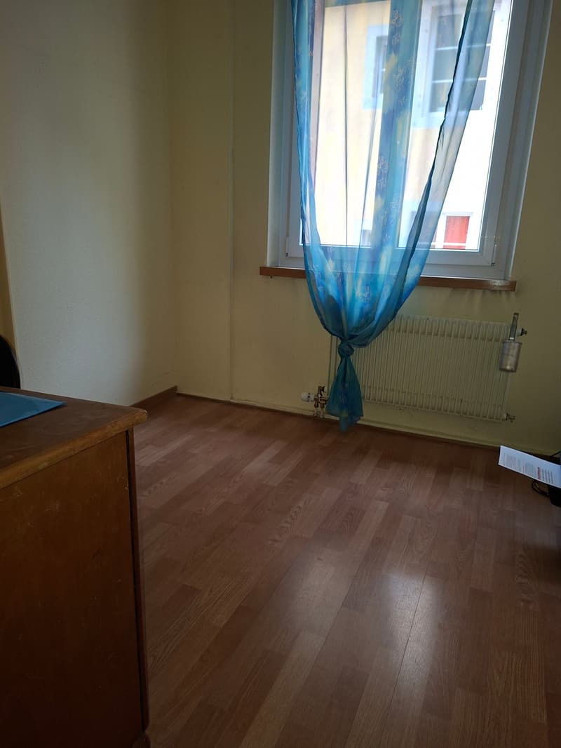 Empty room with wooden floor, large window with blue curtains, wall-mounted radiator, white walls