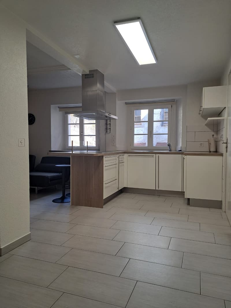Open-plan kitchen and living room. Tiled floor, white cabinetry, central island, stainless steel exhaust hood, wooden countertop, white appliances, open shelves, windows, power outlets, light fixtures, modern design.