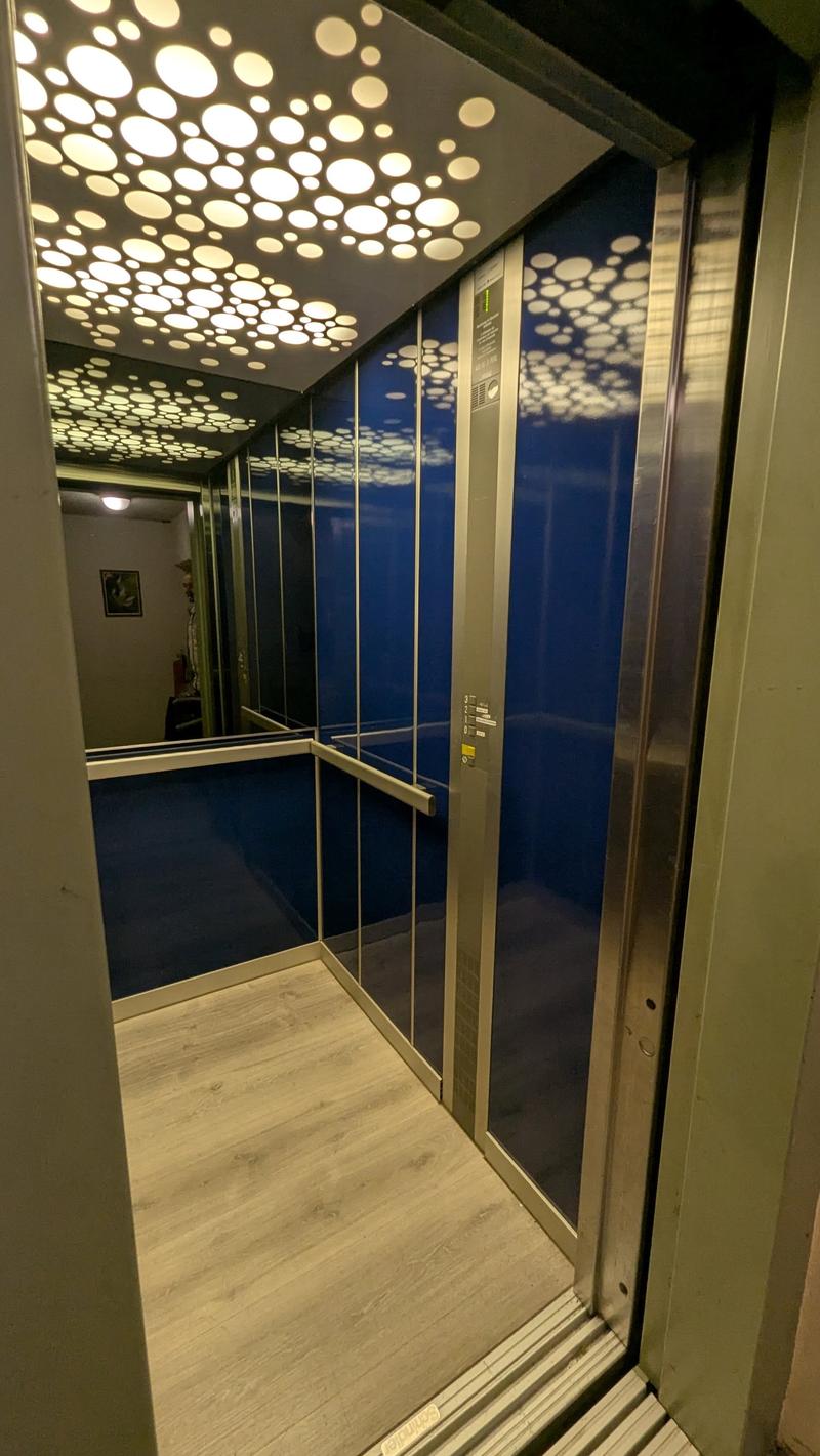 modern elevator with blue walls, wooden floor, silver handrail, ceiling with circular lights