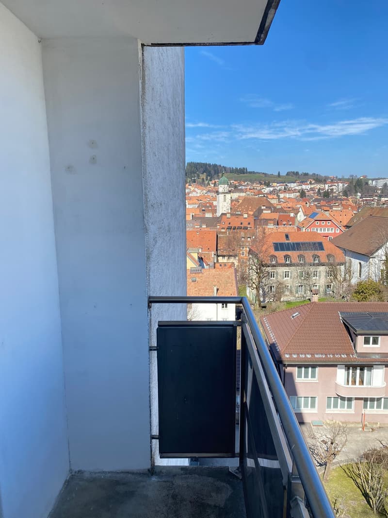 Balcony with metal railing, concrete floor, white wall, view of the city