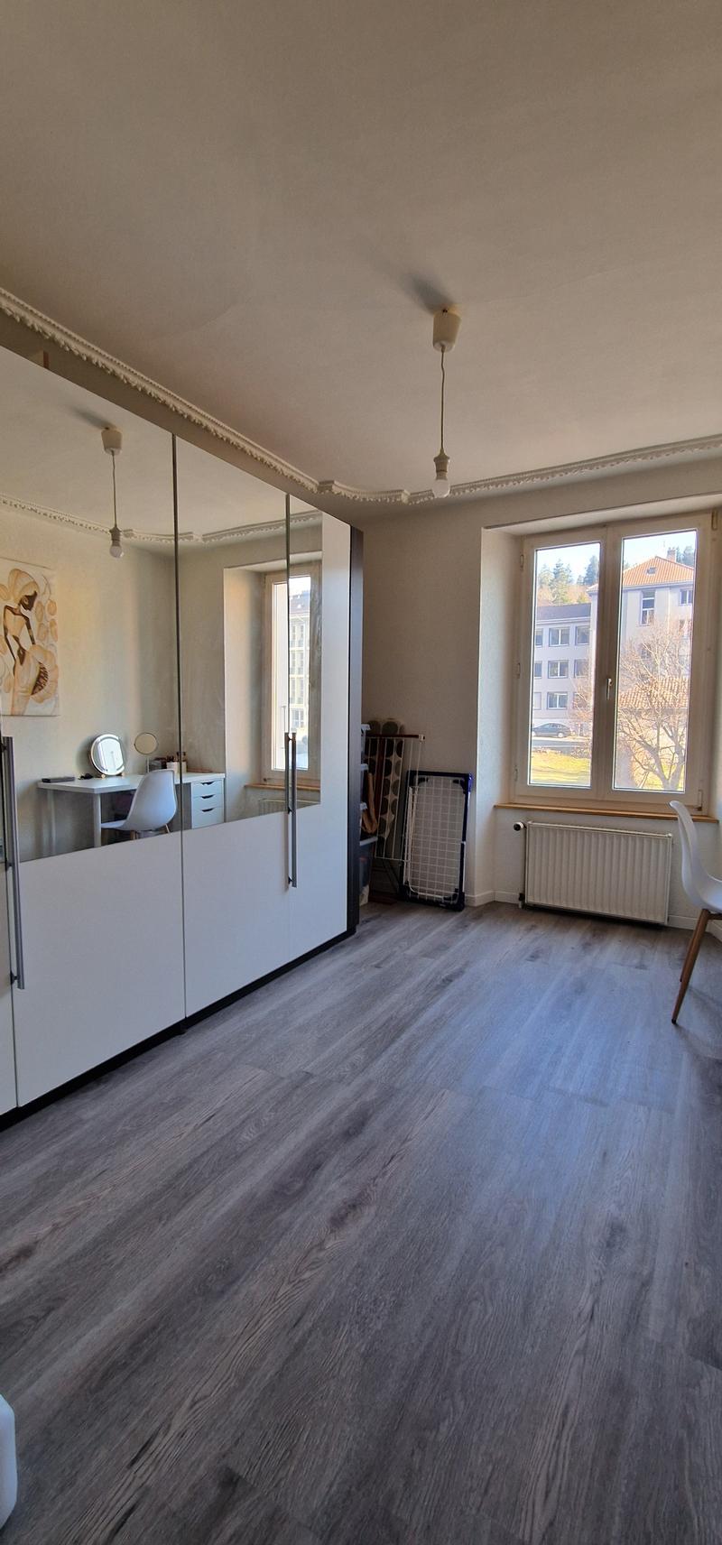large room, wooden floor, large windows, white walls, large mirror, desk, chair, radiator, large windows with view