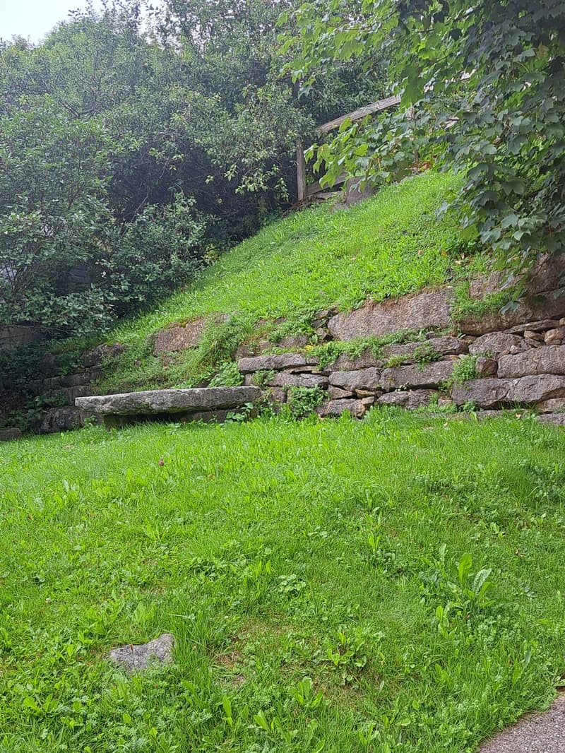 A grassy slope with stone retaining walls and a stone bench