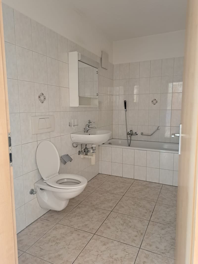 Bathroom with white tiles, white toilet, white sink, bathtub, mirror, and shower head