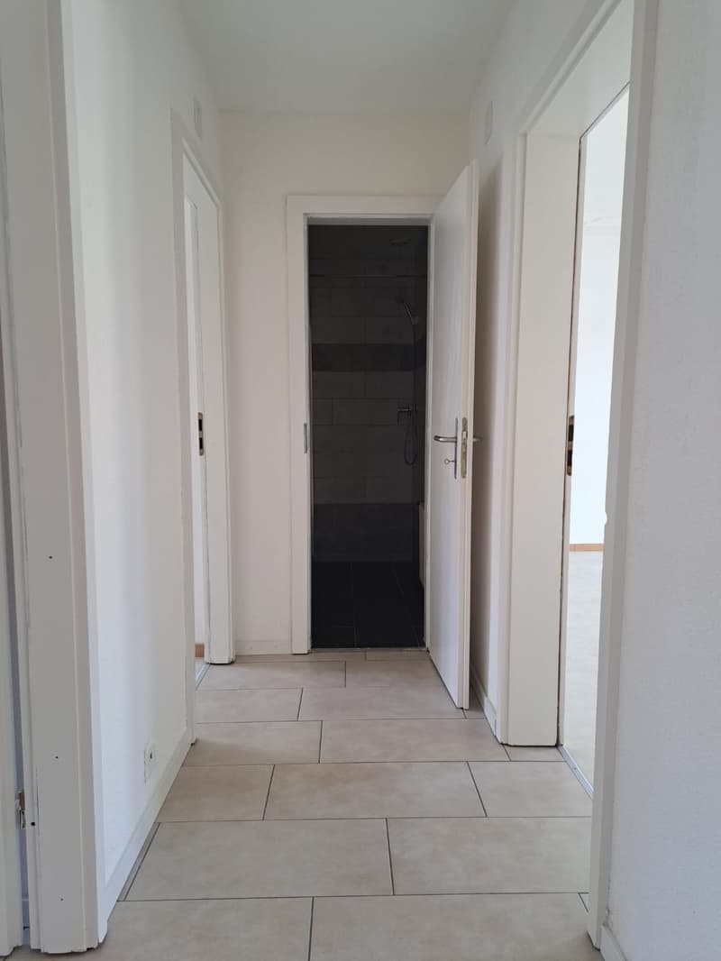 Empty hallway with tiled floor, three doors, one leading to a bathroom