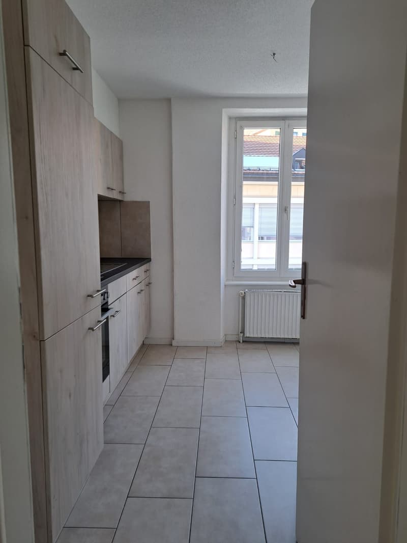 Empty kitchen with white tiles, wooden cabinets, black countertop, window with blinds, white radiator