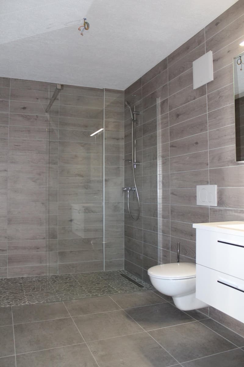 Bathroom with glass shower enclosure, white toilet, white vanity, gray tiles