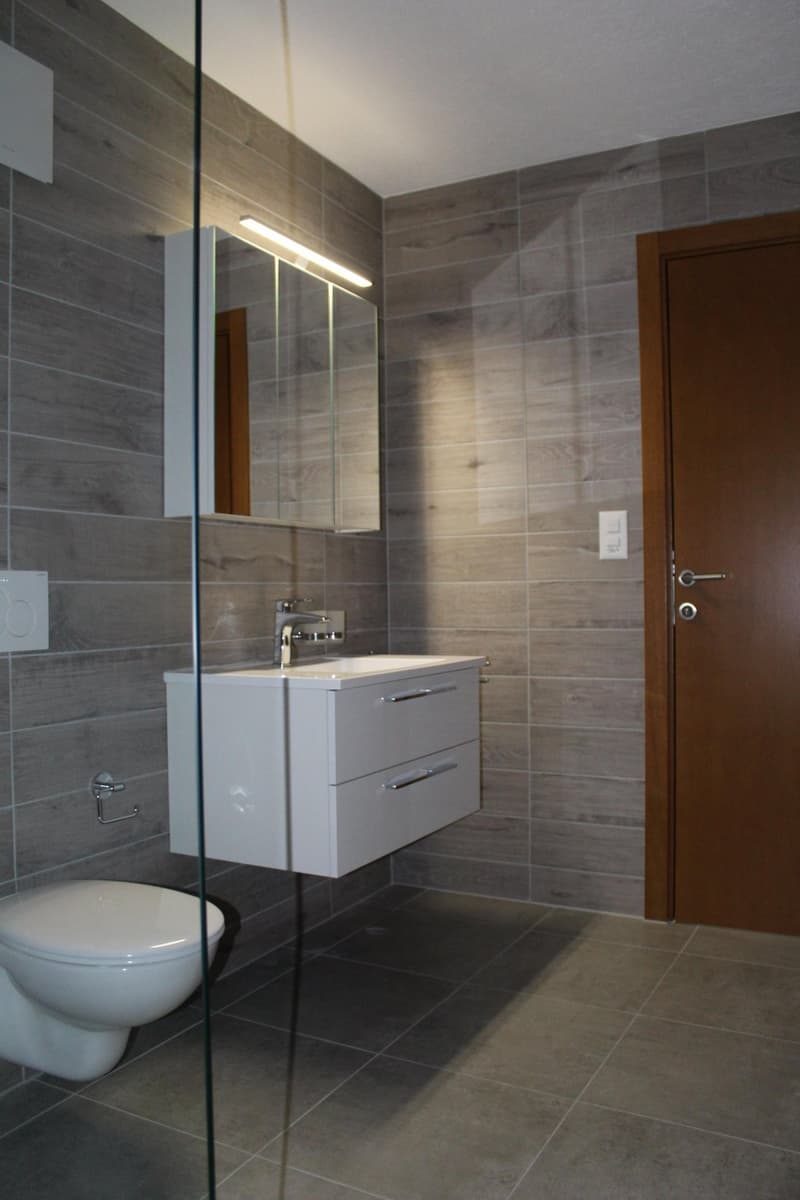 Bathroom with white toilet, white sink, mirror, and tiled walls