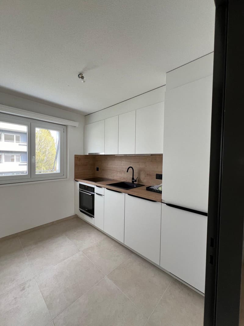 modern kitchen with white cabinets, wooden countertops, black sink, oven, tiled floor, large window