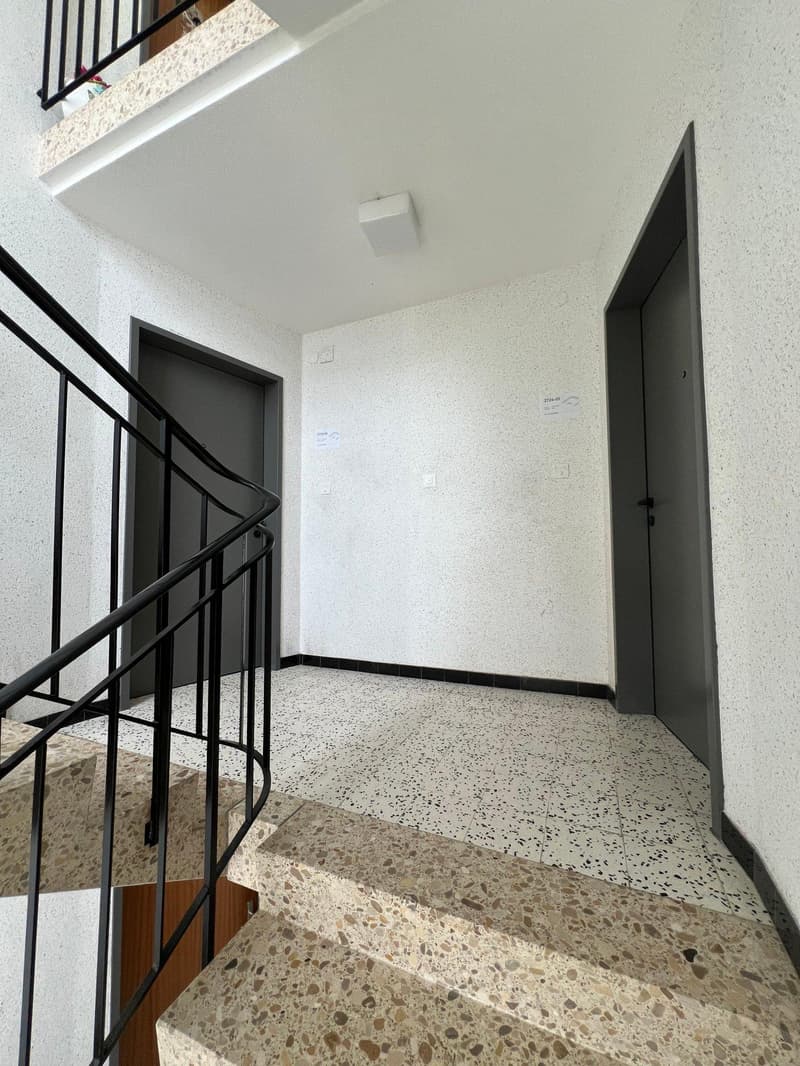 Modern staircase with black handrail, granite steps, and white walls