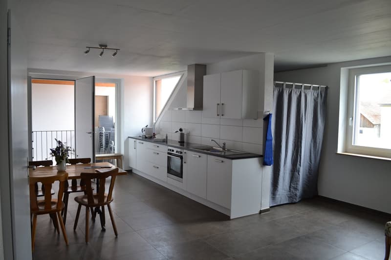 Open-concept kitchen and dining area, white cabinets, stainless steel appliances, wooden dining table and chairs, tile flooring, balcony access