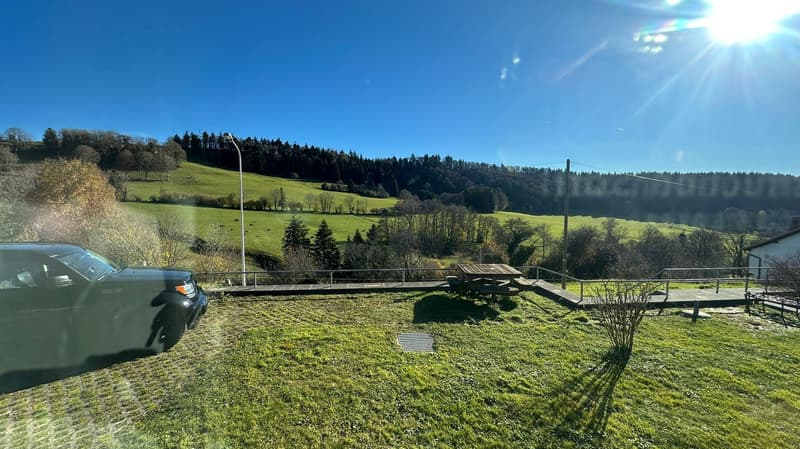 Green grass, table, bench, fence, black car, street light, green rolling hills, clear sky
