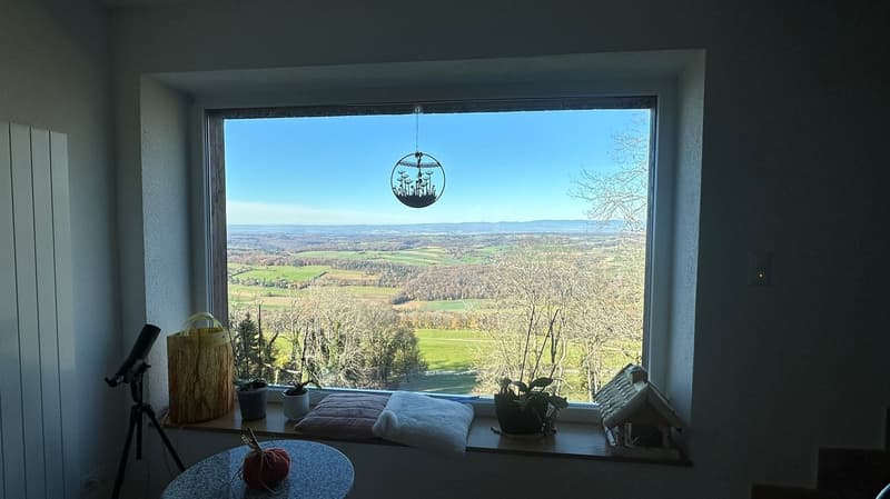 a window overlooking the countryside, window seat with cushions and a small table with a pumpkin