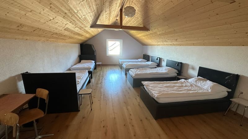 wooden ceiling, wooden floor, several beds, tables, chairs