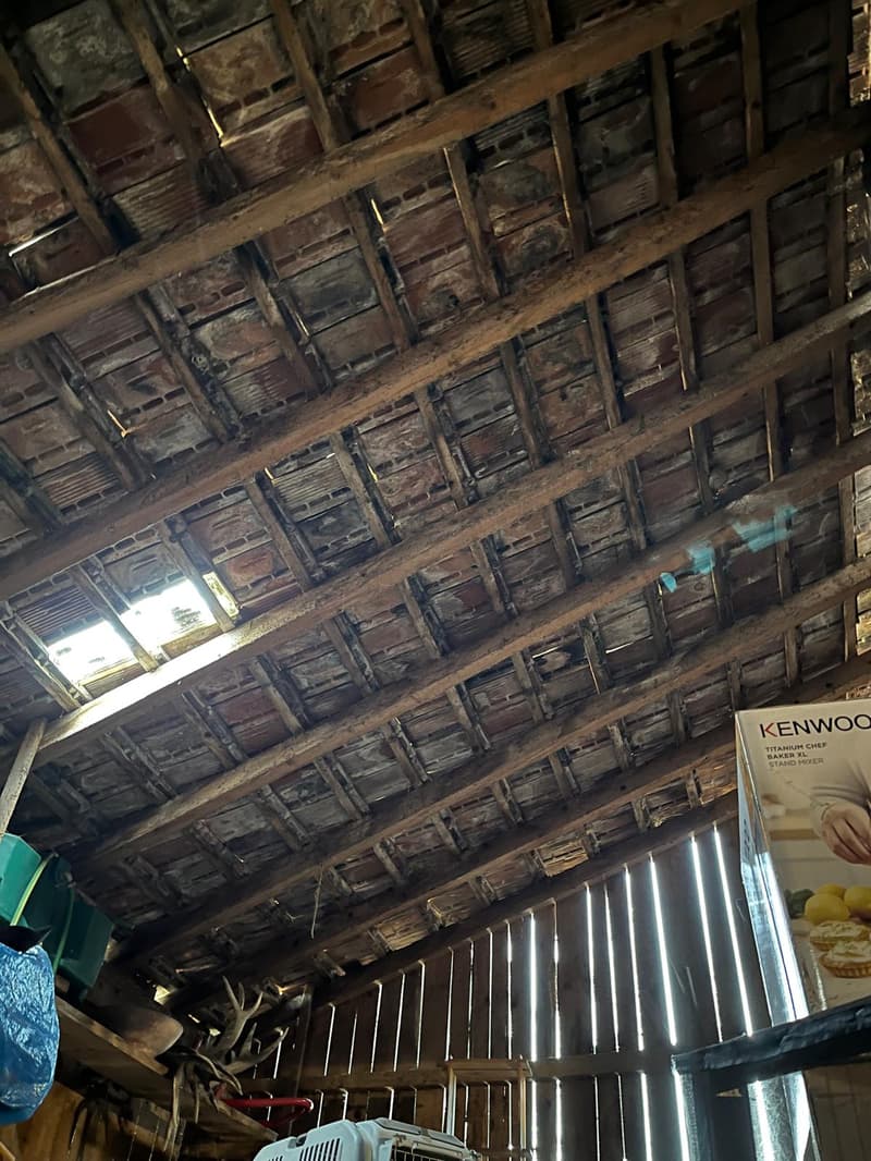 exposed wooden beam ceiling, metal roofing, natural light through a window, various items stored in the corner