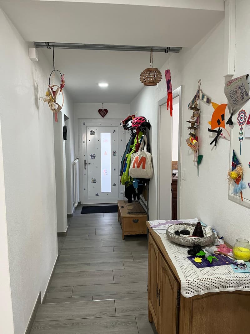 tiled flooring, white walls, entrance door, wooden bench, rack with jackets and bags, various decorative items on the wall