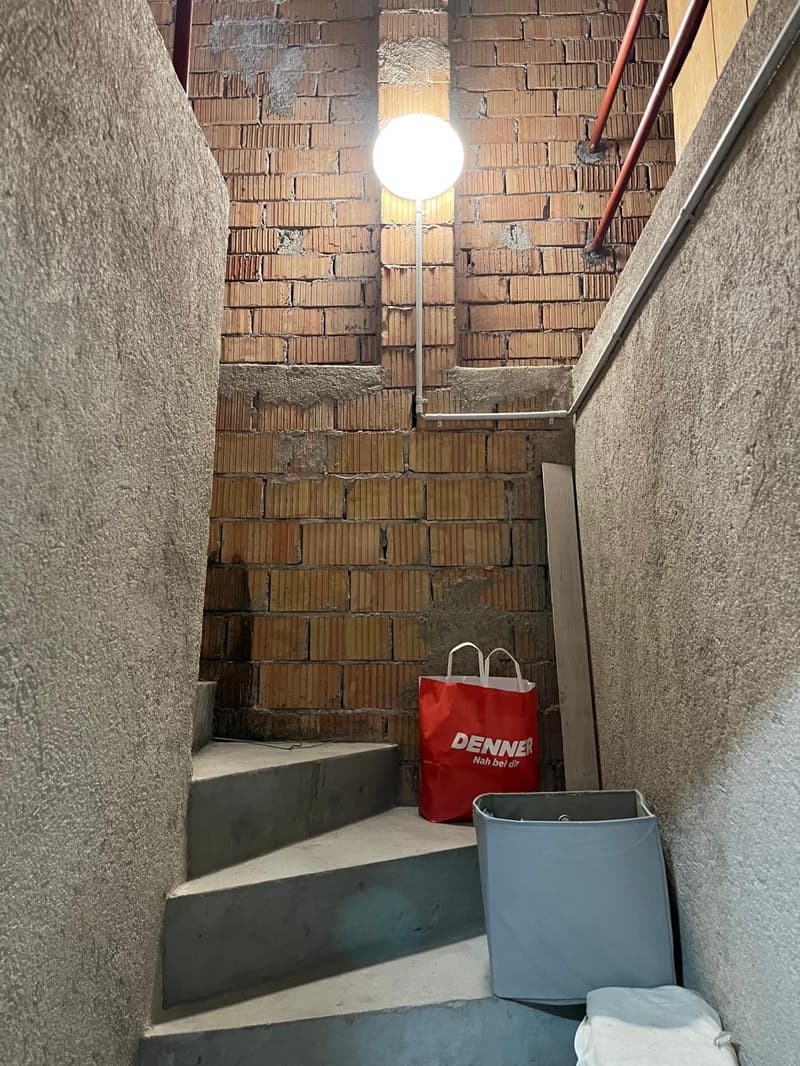 Concrete stairs with a bright light attached to the wall, red brick wall, red Denner shopping bag, grey plastic bin.
