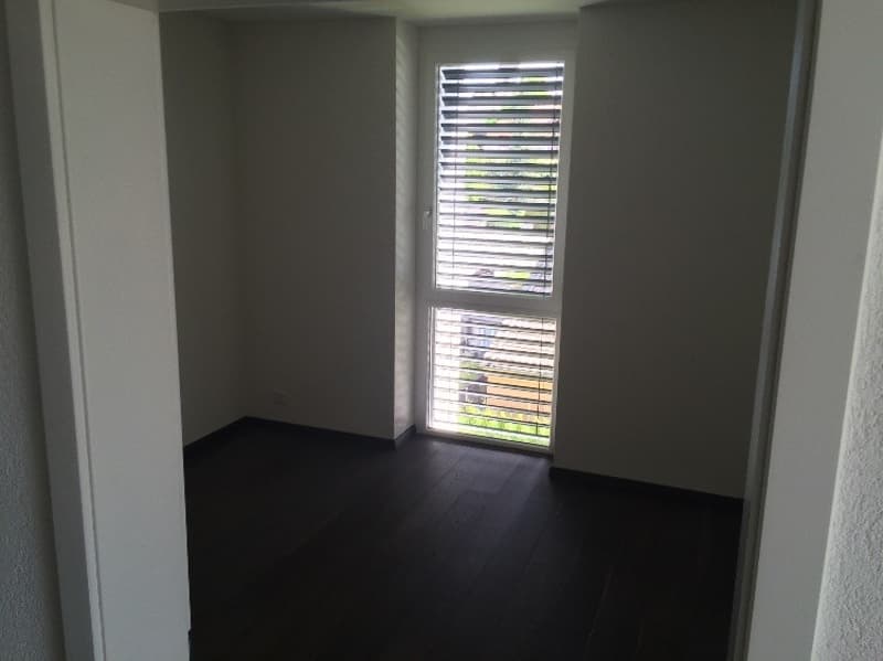 Empty room with white walls, black wooden floor, window with blinds
