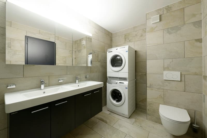 modern bathroom with double sink, mirror, toilet, washing machine, and dryer