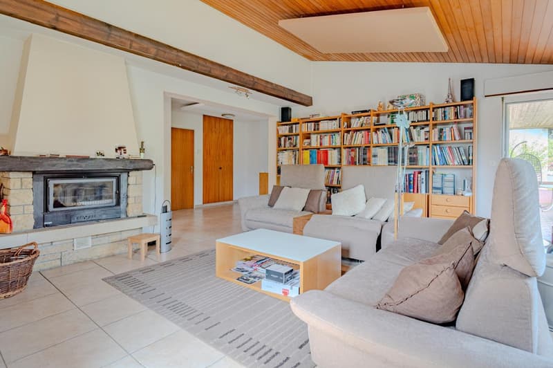 Spacious living room with wooden ceiling, exposed wooden beams, large bookshelves, gray sofas, coffee table, and a fireplace