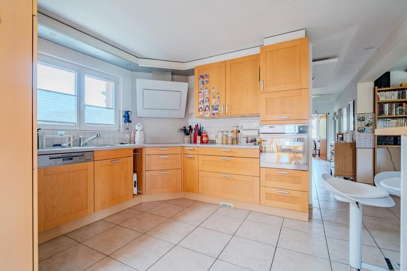 Spacious kitchen with light wood cabinets, tile flooring, appliances including a dishwasher, and various kitchen accessories and decor