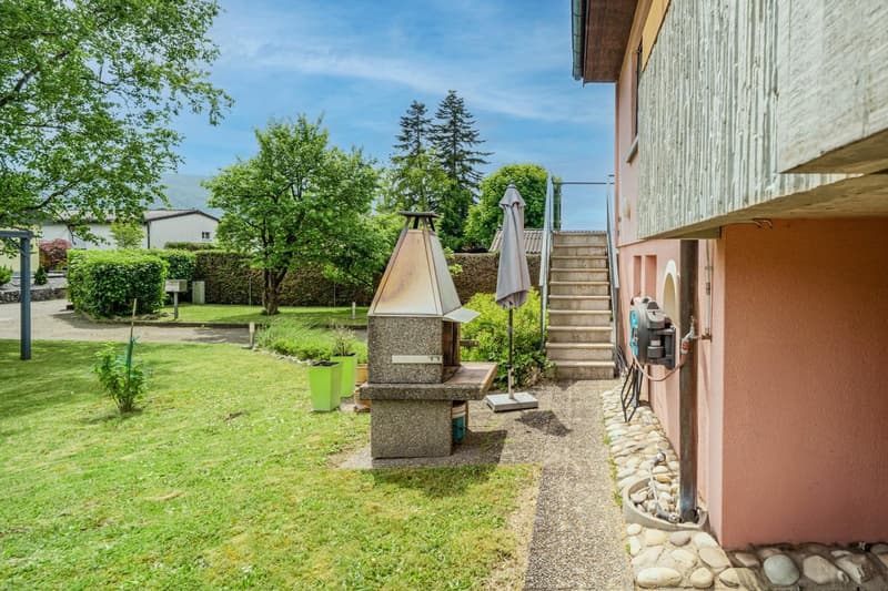 Grassy yard with trees, stone fireplace, stairs leading to a building, and patio umbrellas