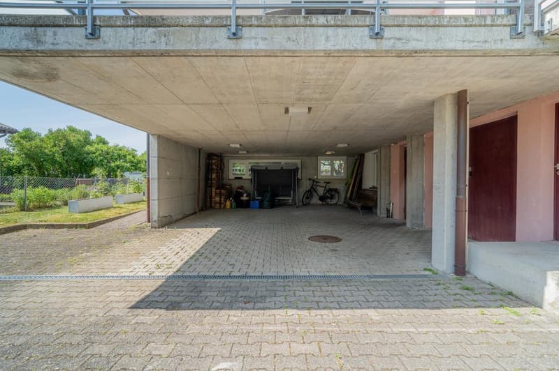 Covered parking area with concrete ceiling and walls, brick paved floor, storage space, and bicycles parked inside