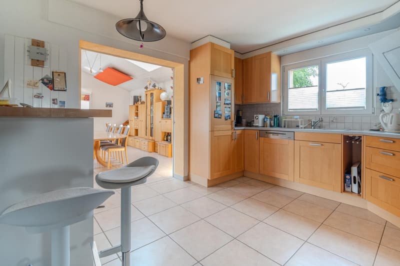 Spacious kitchen with wooden cabinets, tile flooring, and a dishwasher. The kitchen opens up to a dining area with a table and chairs.