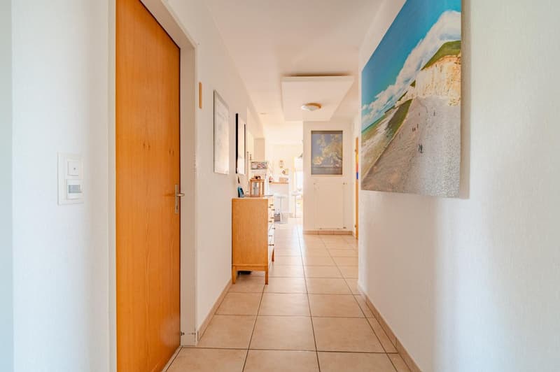 Tiled floor, white walls, wooden doors, artwork on the walls, cabinet in the hallway
