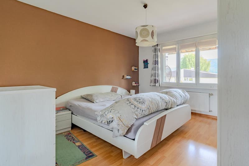 Spacious bedroom with brown accent wall, white bed frame, bedside tables, patterned curtains, and a pendant light fixture.