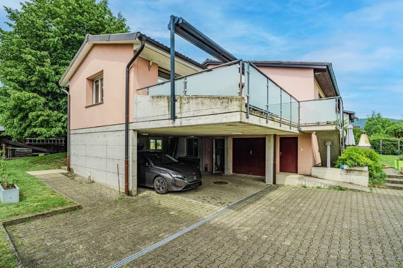 2-story house with a garage and parking space, pink exterior walls, concrete balcony, and a paved driveway leading to the garage doors