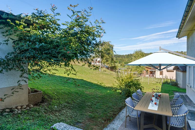 wooden table with 6 chairs and umbrella, gravel path, large green lawn