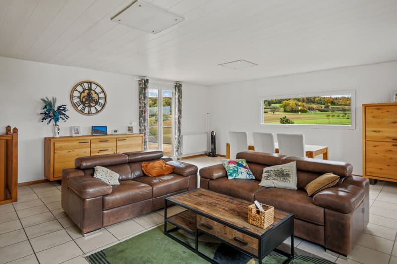 large room, wooden floors, modern couch, wooden coffee table, wooden cabinet, wall clock, large window, balcony, outdoor views