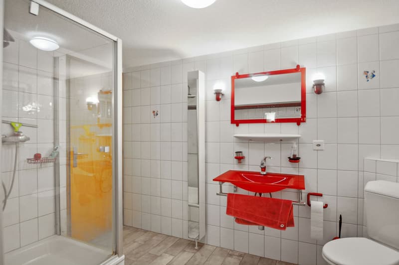 A white and red bathroom with a shower, toilet, red sink, and decorative tiles.