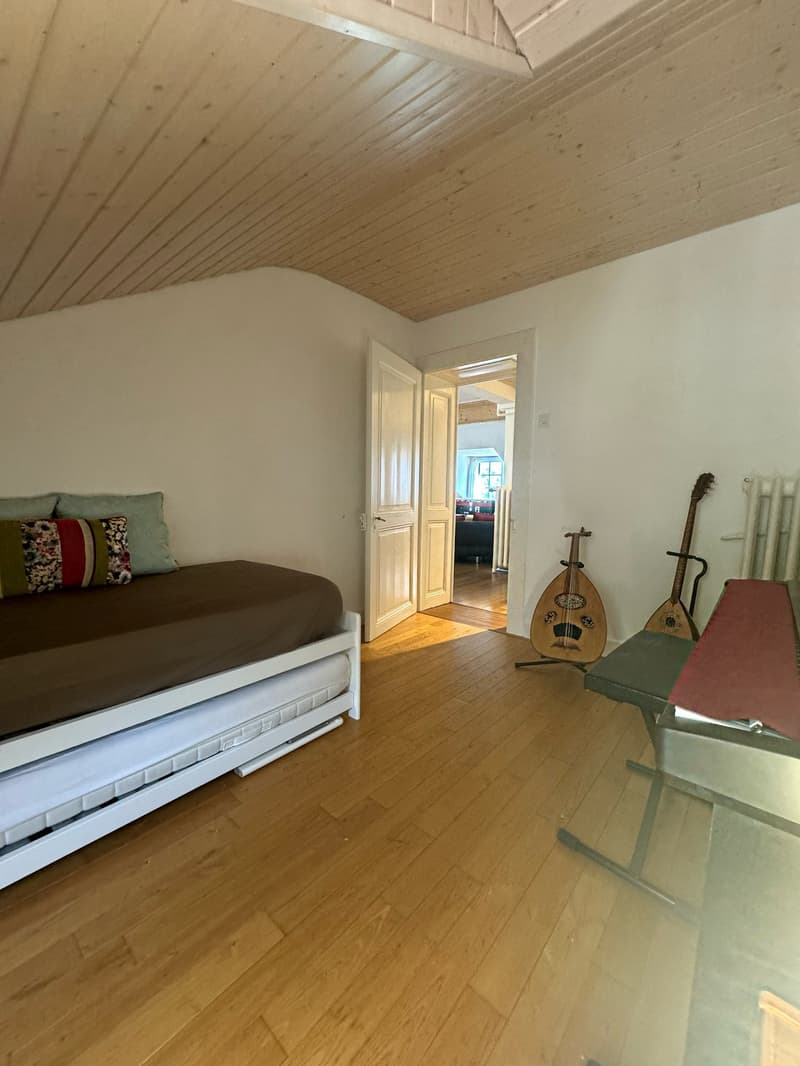 Single bed, two string instruments, white wooden floor, open door, window, white walls, radiator