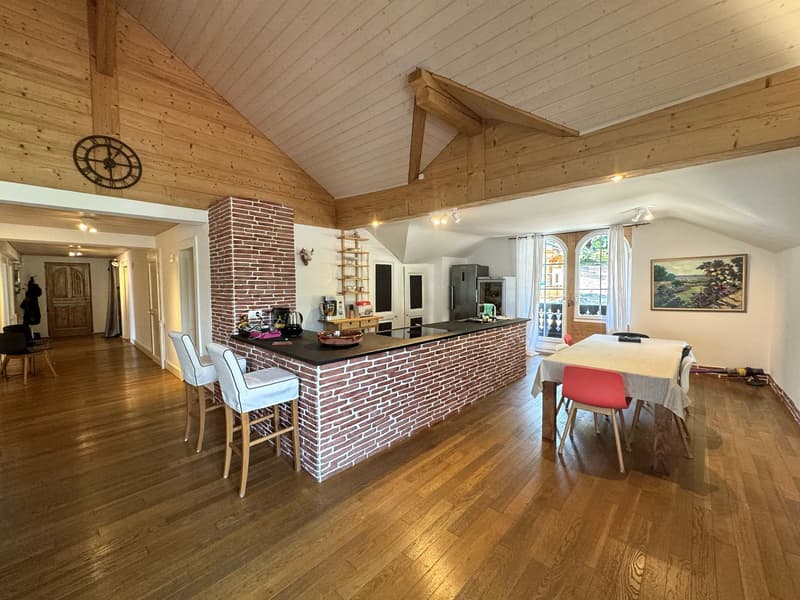 Open kitchen with wooden counter, dining area with table, island with stools, brick fireplace, wooden floor, wooden ceiling