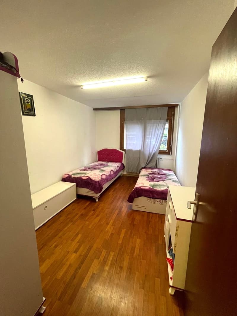 Bedroom with 2 beds, wooden floors, white walls, picture frame, small window, drawers