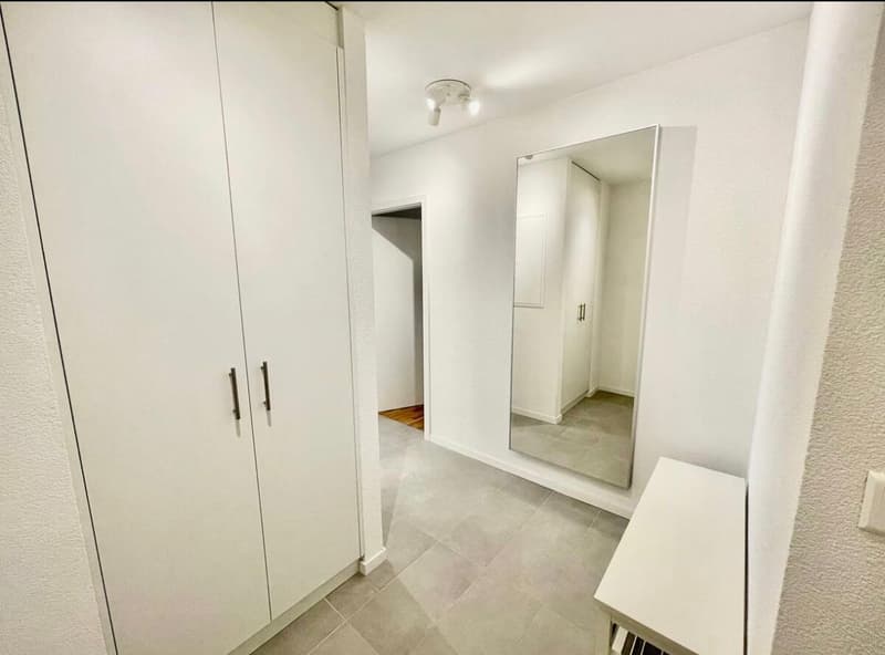 A small room with white cabinets, tiled floor, and a mirror.