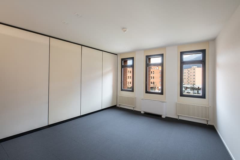 empty room with white walls, black trim, gray tiles, three windows with outside views, radiators