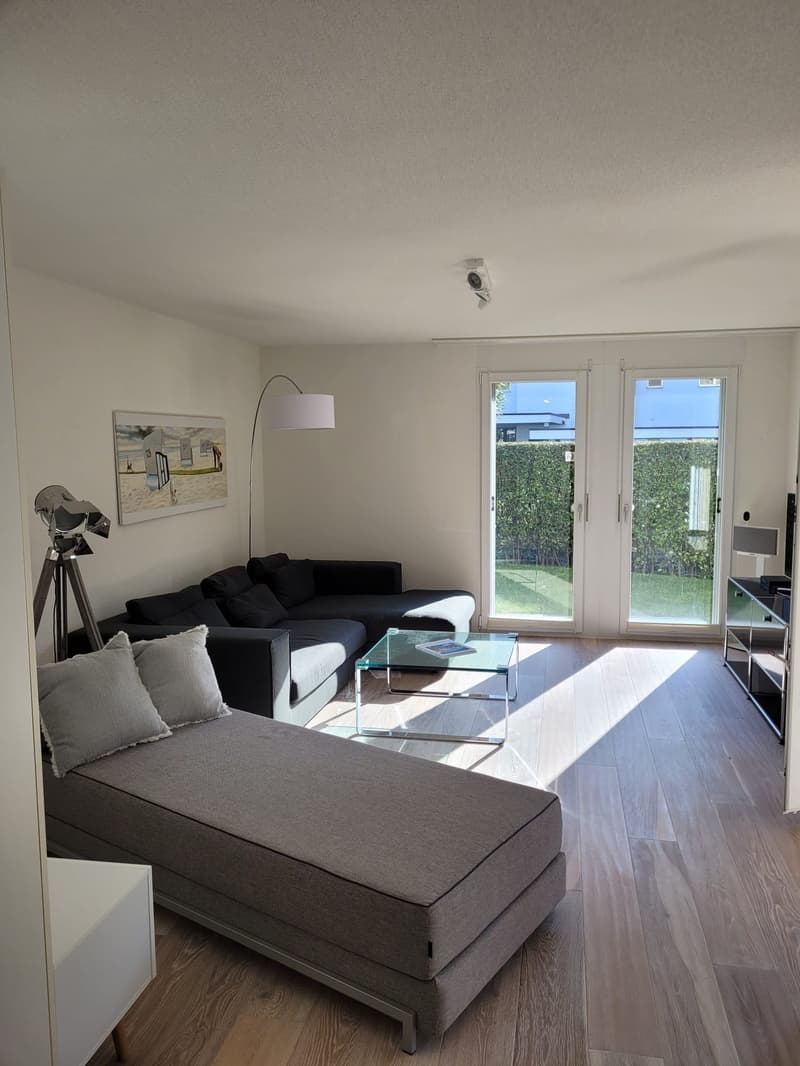 modern living room with a black sofa, glass coffee table, and a glass door leading to a garden
