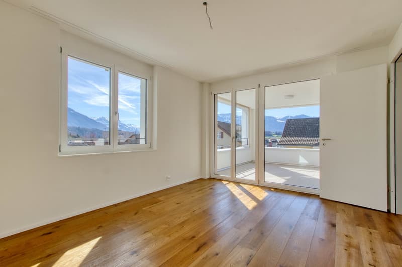 empty room, wooden floor, glass doors leading to balcony, windows with mountain view