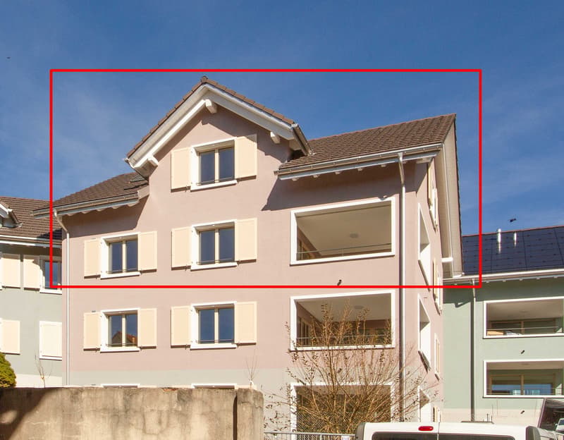 An apartment building with multiple windows, some have balconies. The exterior walls are painted pink.