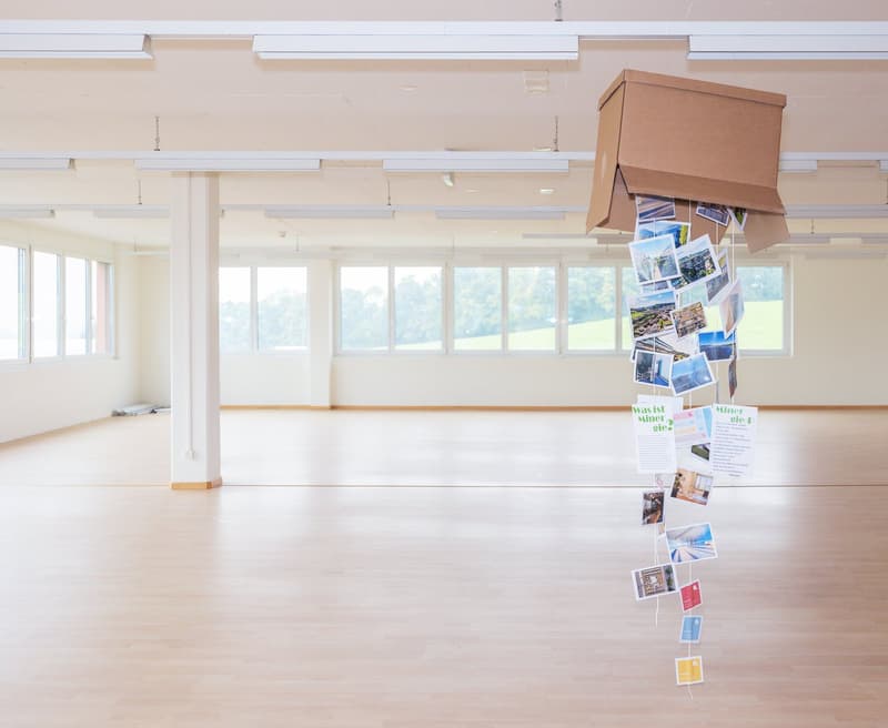 spacious room with large windows, photos and posters hanging, wooden floor, white pillars